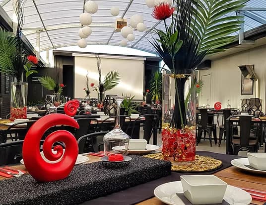 Function room set for dinner with red and black pōhutukawa-themed décor