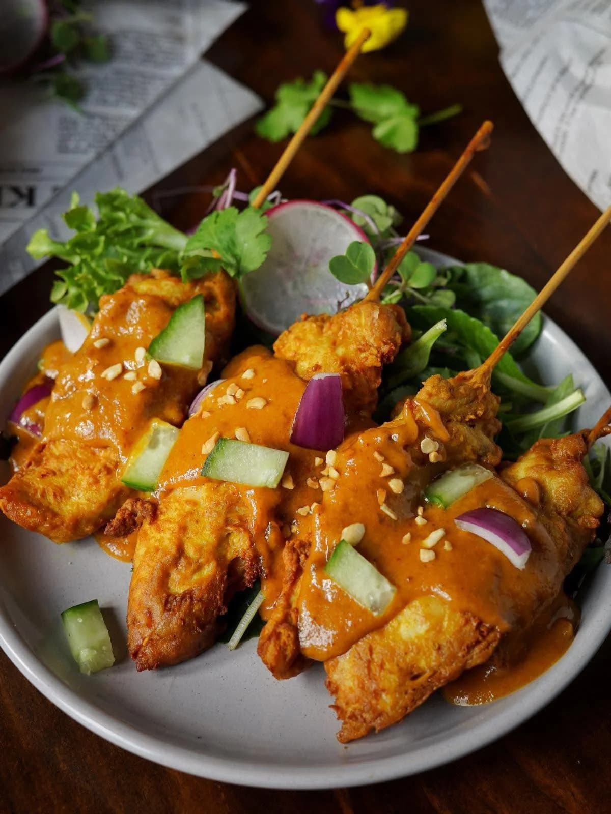 Chicken satay skewers with peanut sauce, cucumber and red onion on a bed of greens