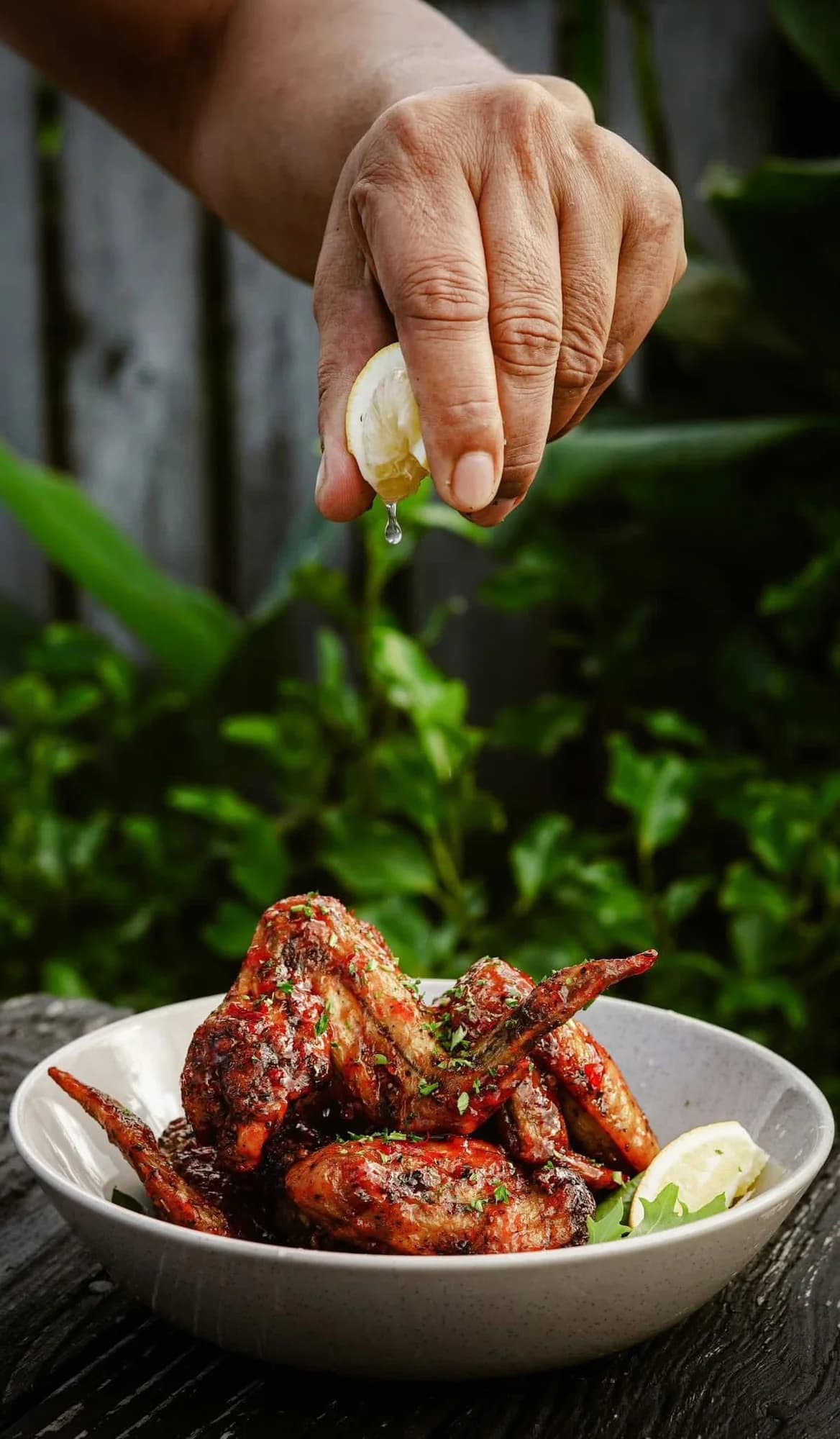 Glazed chicken wings in a bowl with fresh lemon being squeezed over them