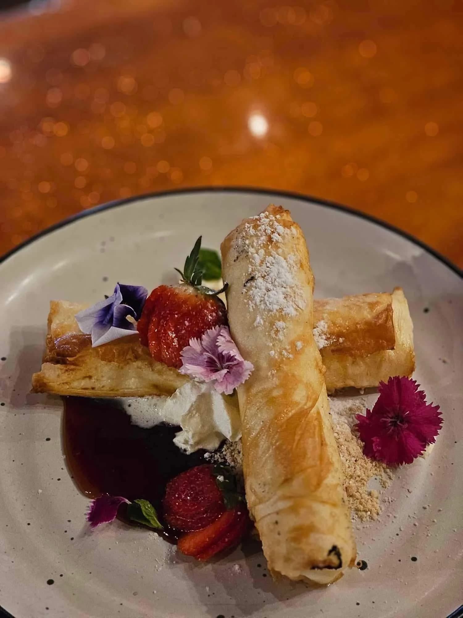 Golden pastry rolls with strawberries, whipped cream, berry sauce and edible flowers