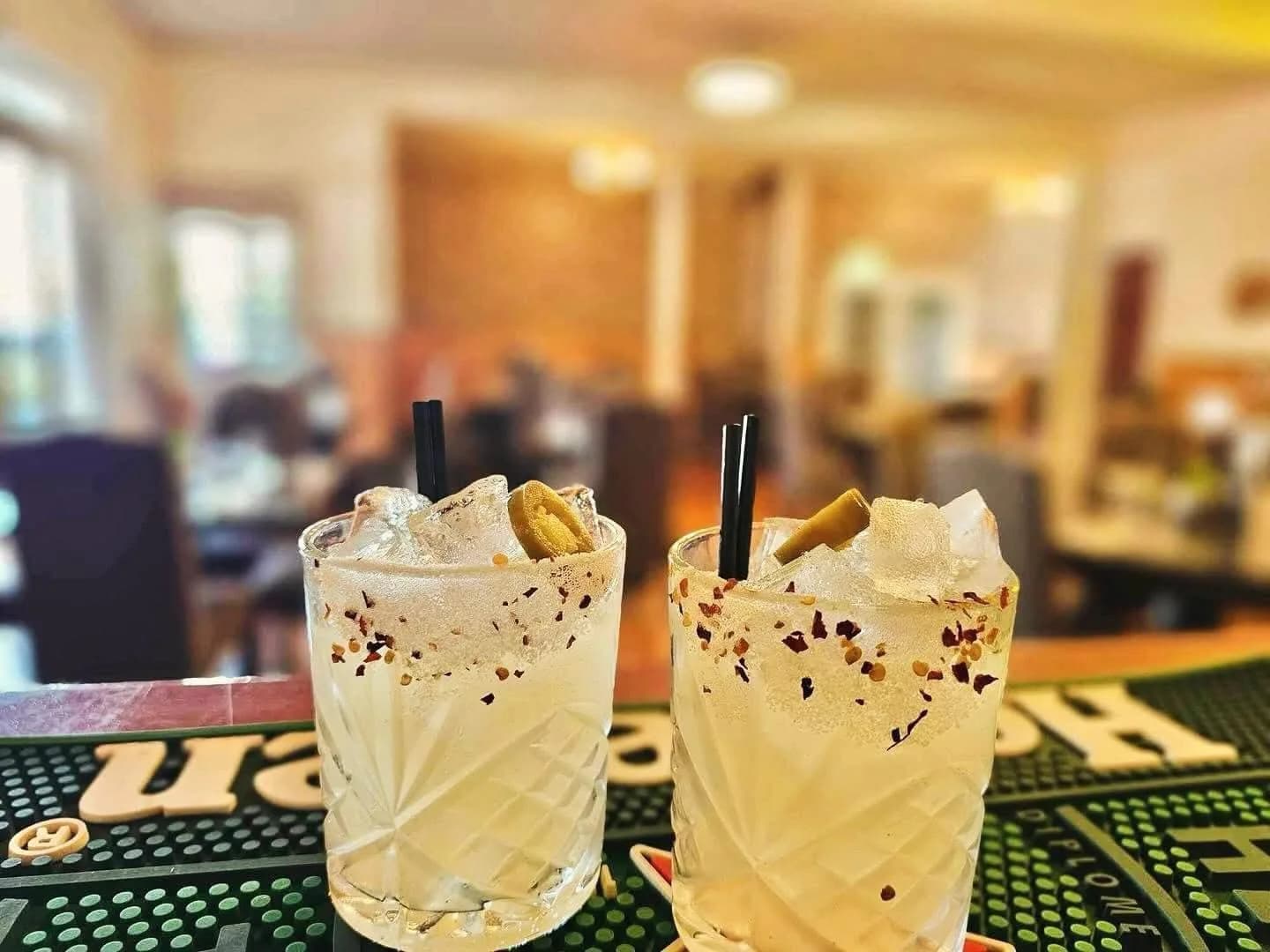 Two spicy jalapeño margaritas with chili-salt rims and jalapeño garnishes on a bar mat