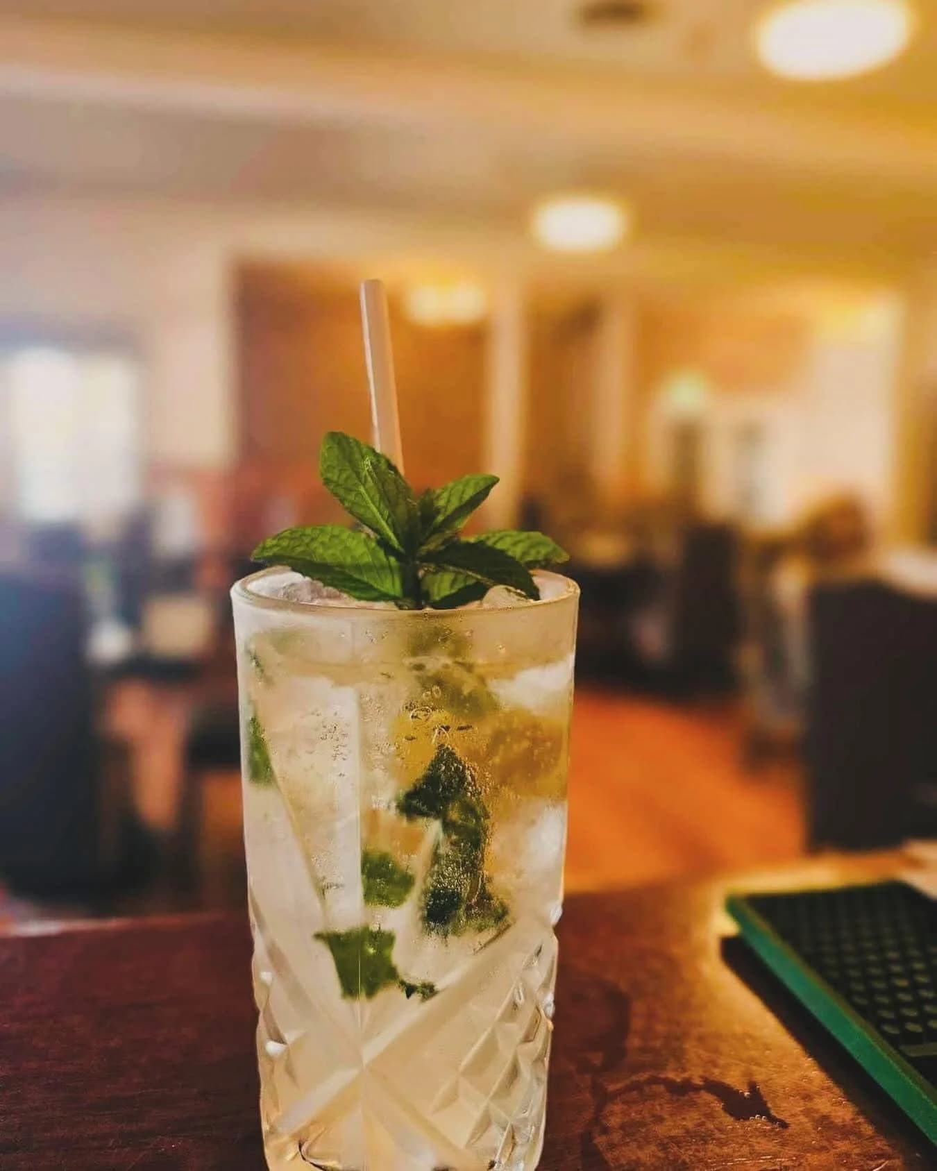 Mojito cocktail with fresh mint on a wooden bar counter with warm restaurant lighting behind