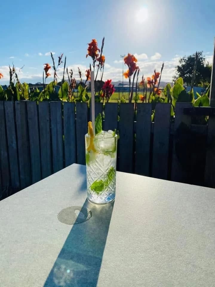 Refreshing cocktail on the sunny outdoor deck with garden flowers and blue sky behind