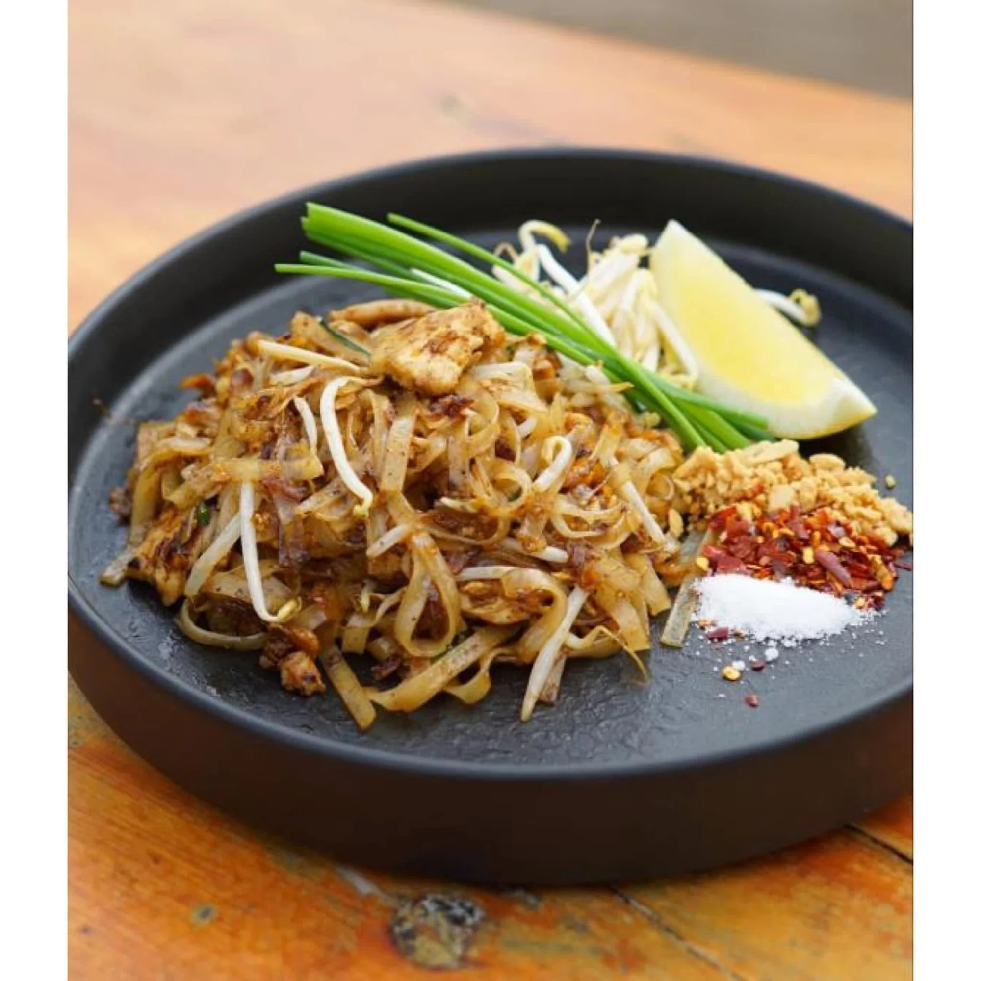 Pad Thai with rice noodles, bean sprouts and condiments on a black plate