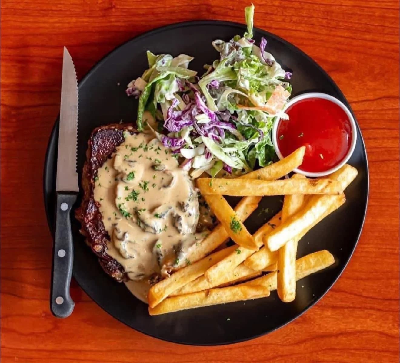 Steak with creamy mushroom sauce, fries and garden salad on a black plate