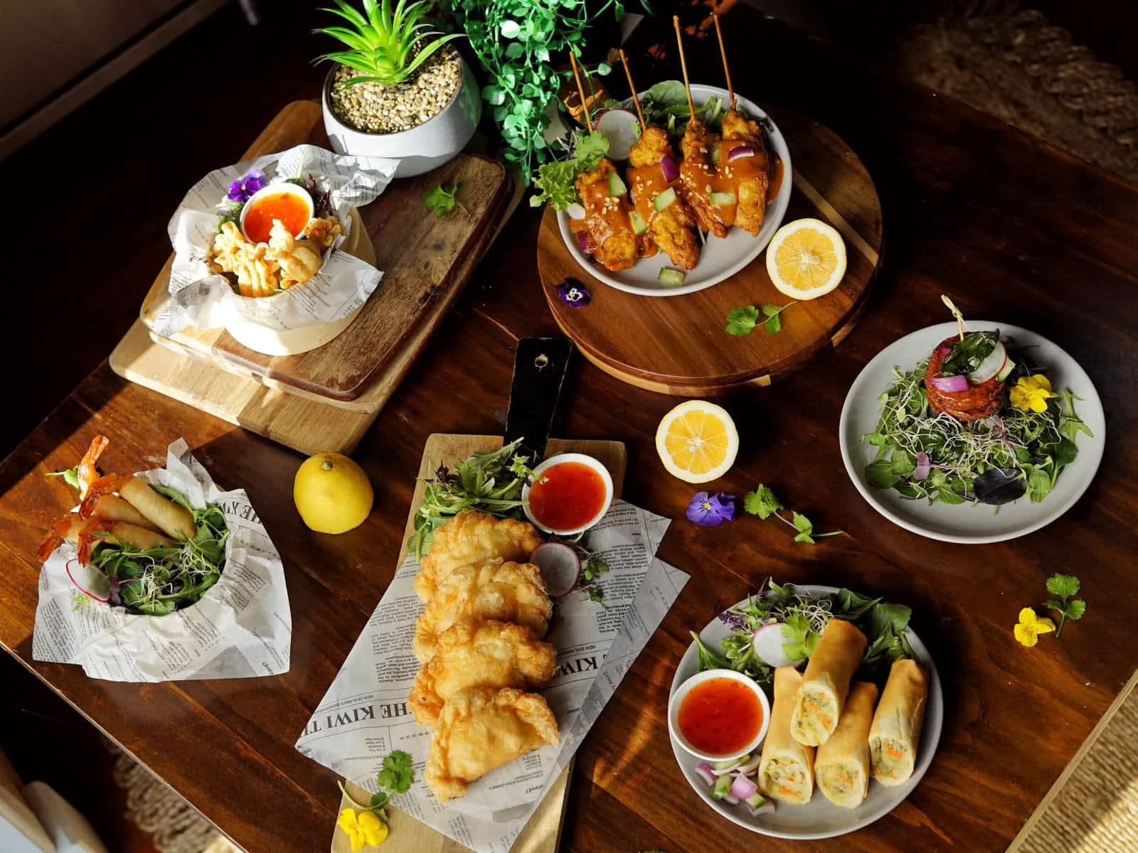 Thai appetizer spread with chicken satay, spring rolls, curry puffs and fried calamari on a dark wooden table