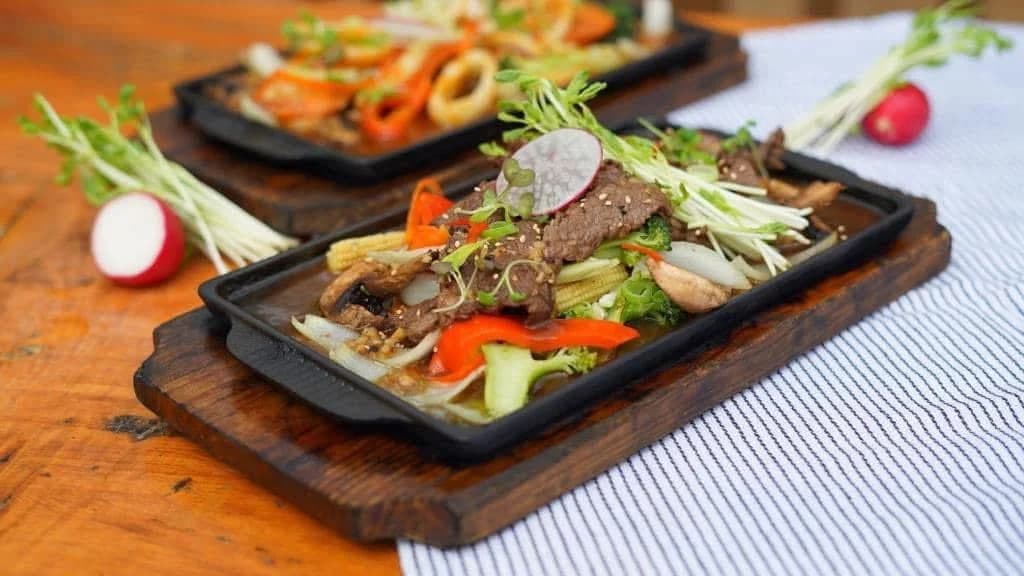 Thai beef stir-fry on a sizzling cast-iron platter with broccoli, peppers and baby corn