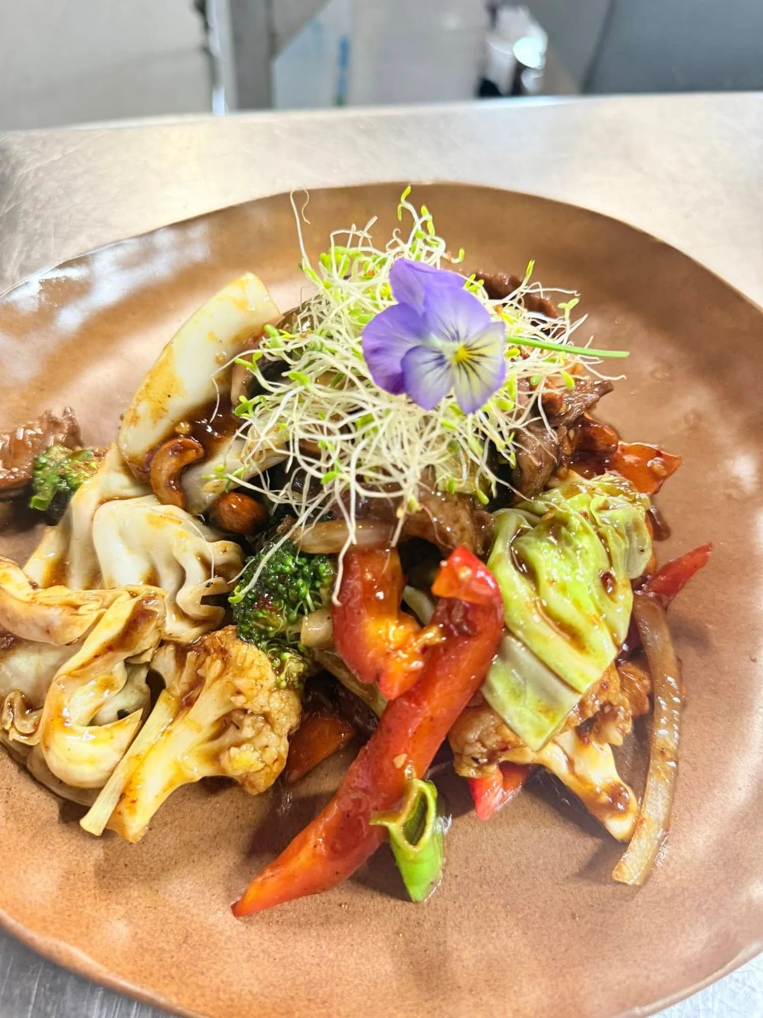 Thai cashew stir-fry with beef, peppers, cabbage and roasted cashews garnished with edible flowers