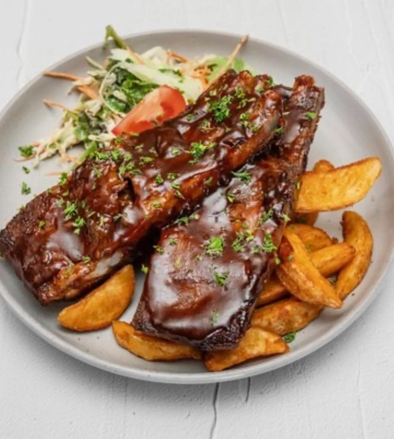 BBQ pork ribs with potato wedges and a side salad on a grey plate